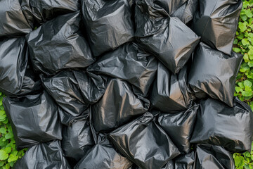 Eco-Friendly Black Trash Bag. A collection of black garbage bags piled together, creating a textured surface against a backdrop of green foliage.