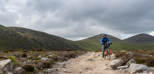 Obraz premium Cyclist man traveling with luggage on bicycle. Mountain landscape, freedom, happiness, inspiration, loneliness, challenge, confidence.