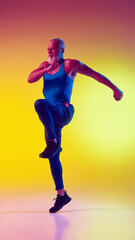 Full-length dynamic image of muscular elderly man in sportswear in motion, training against gradient yellow background in neon light. Concept of sport, active elderly lifestyle, health care