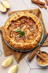 Delicious apple galette decorated with almond petals and cinnamon sticks on white table