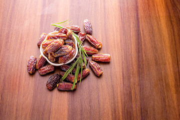Dried dates in wooden bowl and palm leaves on wooden table.