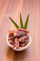 Dried dates in wooden bowl and palm leaves on wooden table.
