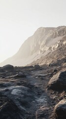 A rocky path leads towards a distant mountain shrouded in mist under a soft, golden light.