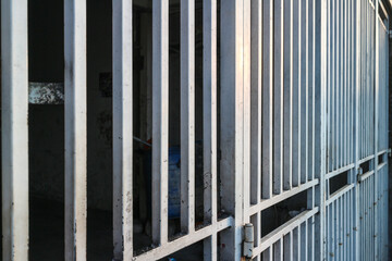 A gray metal gate made up of many thin bars seen from an angle.  Sun shining through the bars casts light and shadows.