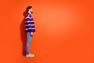 Full size photo of nice young male stand profile empty space wear trendy striped violet outfit isolated on orange color background