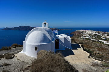 Eine typische Kirche auf der Griechischen Insel Santorin mit Blick bei strahlend blauen Himmel auf die Stadt Oia.