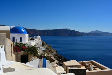 Eine Panoramaaussicht von Oia auf der griechischen Insel Santorin, zu einer der bekannten blauen Kuppelkirchen und den weiteren verlauf der Caldera bis nach Fira.