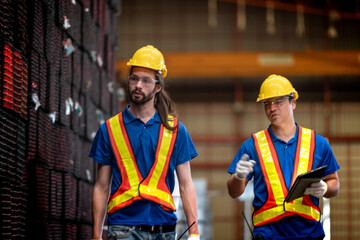 Two construction workers, wearing yellow helmets and reflective vests, collaborate in an industrial setting. They review information on a tablet, emphasizing teamwork, technology, and workplace safety