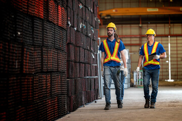 Two construction workers, wearing yellow helmets and reflective vests, collaborate in an industrial setting. They review information on a tablet, emphasizing teamwork, technology, and workplace safety