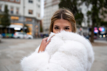 Fashion model hiding face with white fur coat in the city