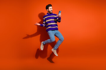 Obraz premium Full size photo of nice young male excited jump hold device wear trendy striped violet outfit isolated on orange color background