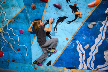 Obraz premium A 10-year-old boy climbing on a colorful indoor bouldering wall, focused on reaching the next hold. Active lifestyle and sport for kids.