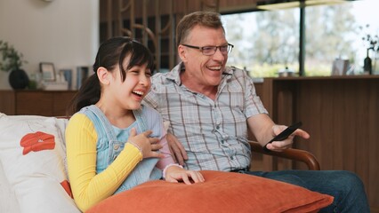 Grandfather and granddaughter together watch interesting entertainment media on TV. Old senior use technology communicate with young generation cross generation gap strengthen family bond. Divergence.