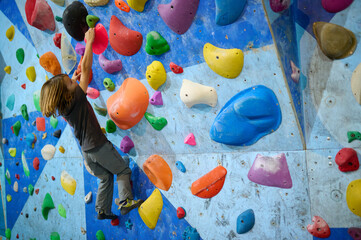 A 10-year-old boy climbing on a colorful indoor bouldering wall, focused on reaching the next hold. Active lifestyle and sport for kids. © sandsun