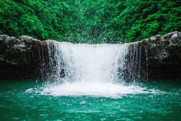 A stunning waterfall cascades into a serene turquoise pool, surrounded by lush green foliage, creating a tranquil and picturesque nature scene.