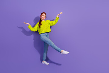 Young red-haired woman in vibrant green sweater joyfully poses against a purple backdrop, expressing a sense of exuberance and style