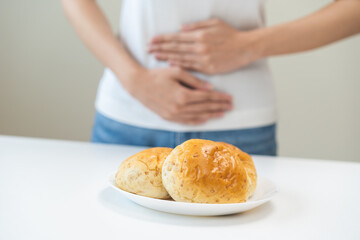 Gluten allergy, asian young woman, girl having a stomach ache hand holding, refusing to eat white loaf slice on plate in breakfast food meal at home. Gluten intolerant and Gluten free diet concept.