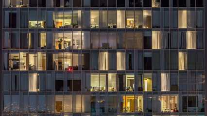 Windows of the multi-storey building of glass and steel lighting inside and moving people within timelapse