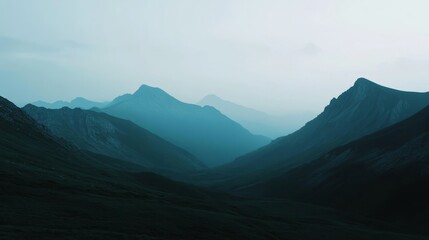 Fototapeta premium Tranquil mountain scene with misty valleys and towering peaks, captured at dawn under a serene blue sky.