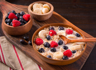 Steel cut oats with raspberries, blueberries, almond mile, and banana in a brown bowl with a wooden spoon; plant-based diet