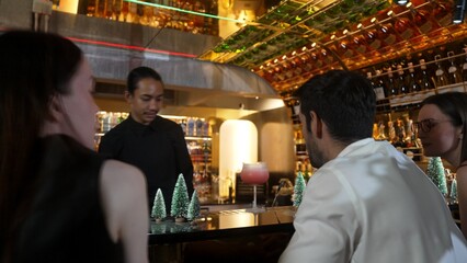 Asian bartender using strainer all ingredients alcohol liquor and syrup tasty in cocktail glass at decorated christmas trees serving refresh drink to VIP couple guest nightlife at nightclub. Vinosity.