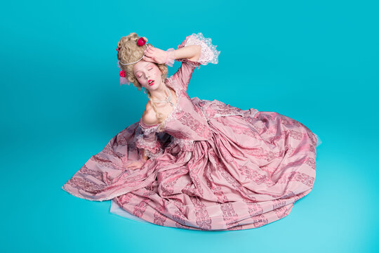 Photo of adorable lady princess wear pompous pink ruches gown sit floor faint feel bad isolated on blue color background