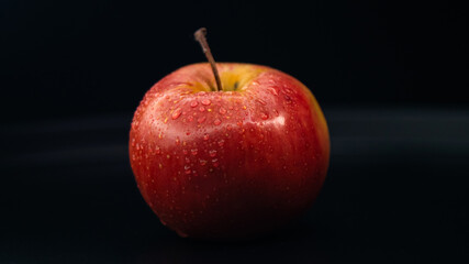 A fresh red apple covered with water droplets, isolated on a black background to emphasize juiciness.