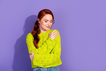 Charming young woman with red hair in green sweater against purple background, conveying warmth and...