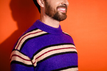 Smiling young man wearing striped sweater against vibrant orange background, showcasing bearded style and cheerful mood