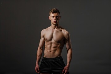 Fototapeta premium A confident young man stands shirtless in sleek underwear highlighting his perfect muscular body. The neutral grey backdrop emphasizes his fitness and dedication to health and beauty.