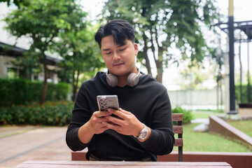 Fototapeta premium Portrait of Handsome Young Asian Man Sitting Outdoors in Park