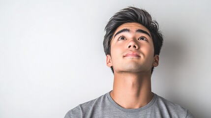 Fototapeta premium Young man with dark hair gazing upwards, reflecting thoughts and aspirations, in a minimalist setting with subtle, neutral background tones.