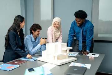 Diverse team of professionals gathered around a table, discussing an architectural model and plans during a creative office meeting.