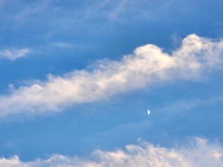 waxing moon in blue sky during daytime between white clouds