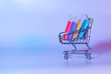 Trolley cart and colorful shopping bags on neon background. Creative idea for shopping online, summer sale, e-commerce, black friday, cyber monday concept.