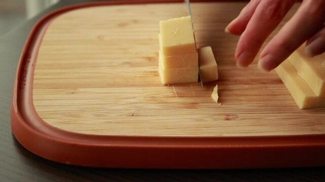 Slicing Aged Cheddar or Parmesan into Cubes on Wooden Board Close-Up
