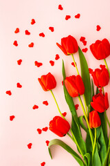 Fresh red tulips and hearts on pink background, concept of spring and holidays or Valentine's Day, top view, copy space