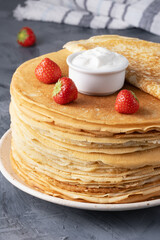 Pancakes with sour cream and strawberries on a grey table
