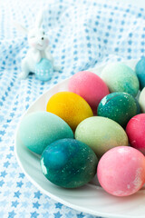 Multi-colored Easter eggs in an oval dish with decorative bunnies on a blue tablecloth, Happy Easter holiday