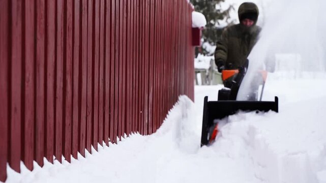A man removes snow with a snow blower in the yard