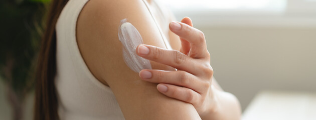 Health skin care, beauty smile asian young woman, girl  hand applying, putting moisturizer on her arm, shoulder after shower bath at home. Skin body cream moisturizing lotion, routine in the morning.