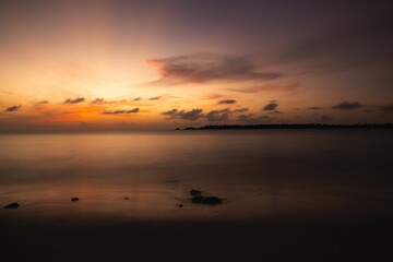 Tranquil sunset over a calm ocean with soft clouds and a distant shoreline
