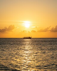 Silhouette of a boat on the ocean at sunset with golden sky and shimmering water