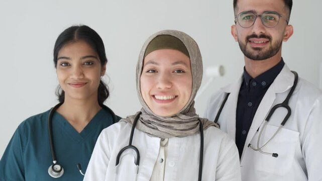 Pretty islamic muslim happy female doctor standing next to colleagues doctors. Medical services and insurance. Arabian Middle Eastern mixed race doctors interns staff