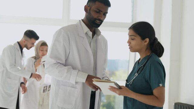 Two doctors workmates using paper review patient anamnesis, share opinion about further treatment, engaged in teamwork, learn new telemedicine program for easy remote consulting to clinic clients