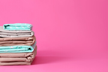 Stack of clean bed sheets on pink background. Space for text