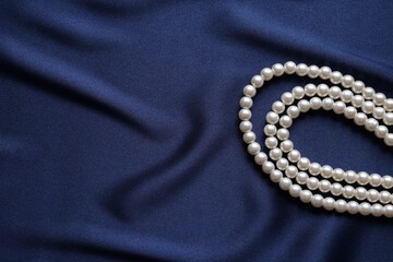 Elegant pearl necklace on dark blue fabric, top view. Space for text