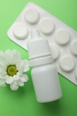 Allergy treatment. Nasal drops, pills and flower on green background, flat lay