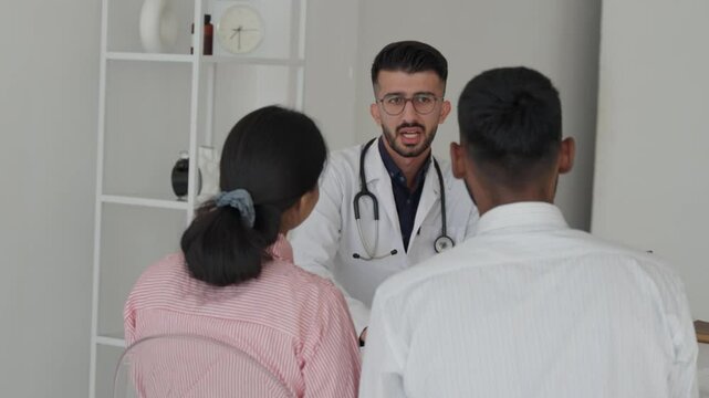 Male doctor advise couple about planning to have children, Couple having consultation with a doctor and talking to each other at medical clinic. Indian man doctor appointment with indian family 