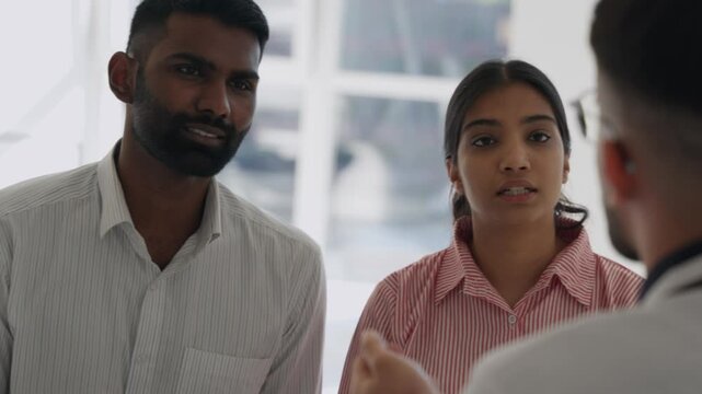 Doctor consulting young married indian couple, getting bad news about health problems, infertility, difficult therapy need. fertility specialist in uniform provide consultation, explain treatment plan